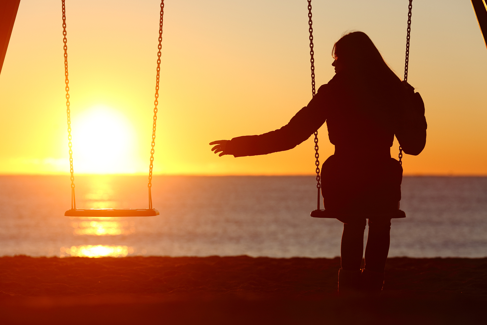 Single or divorced woman alone missing a boyfriend while swinging on the beach at sunset